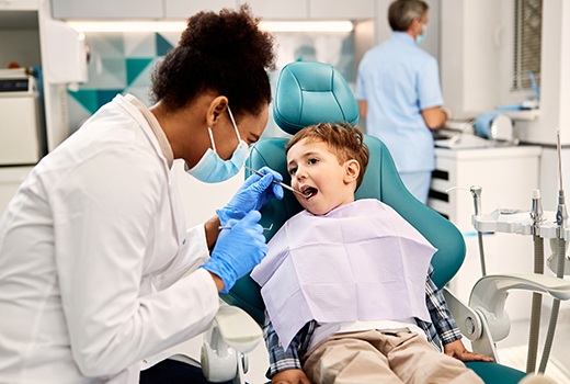 Little boy in pink bib getting teeth examined by dentist