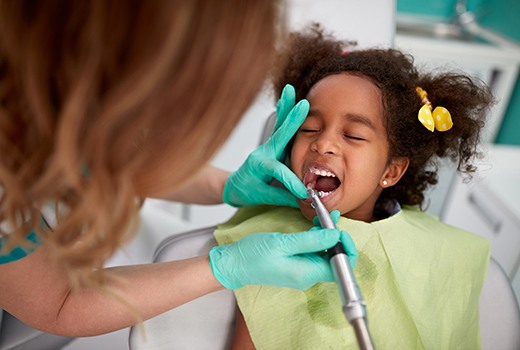 Girl in yellow bib closing eyes while teeth are polished