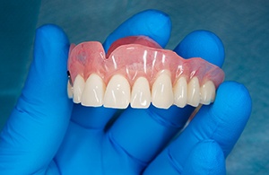 A closeup of a gloved hand holding a full denture
