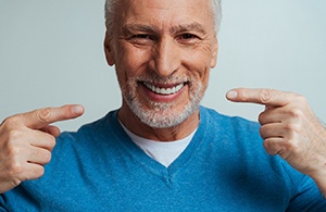 A handsome older man pointing to the dentures he’s wearing