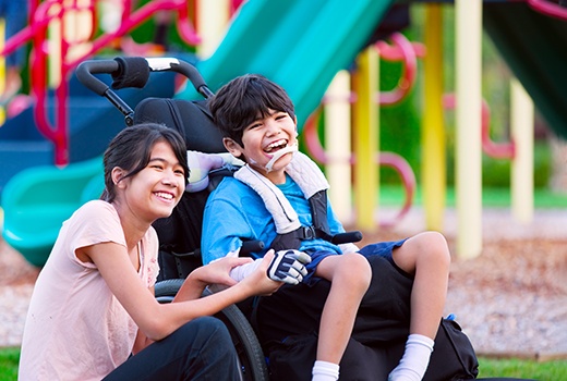 child with special needs in a wheelchair holding his sibling’s hand at the playground