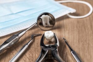 An extracted tooth held by forceps reflected in a dental mirror by a mask on a table